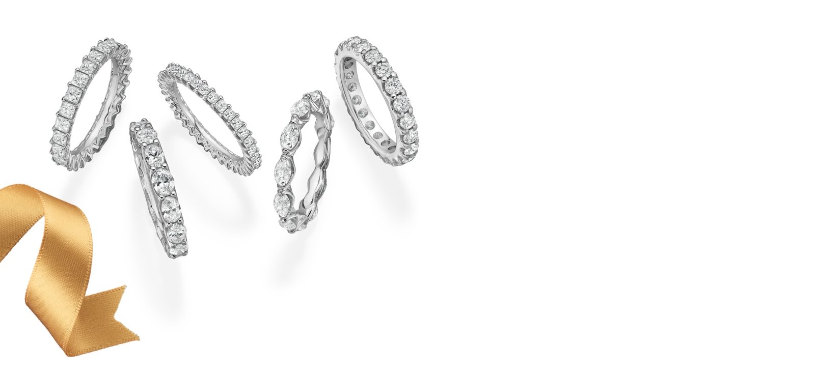 Five diamond eternity bands with princess, round, marquise, emerald and cushion cut diamonds set in white gold on a white background and a gold ribbon.
