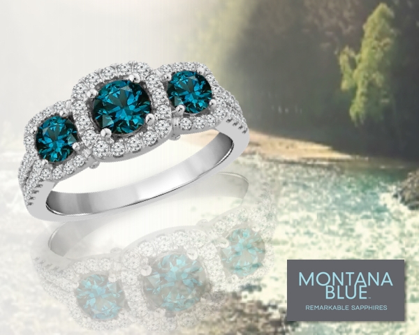 3-stone Montana Blue™ sapphire ring set in white gold over a Montana tree and river landscape background image that fades to gray.
