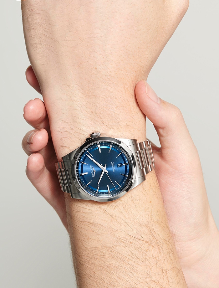 Men&#39;s wrist wearing a Longines watch with round blue dial, white markers and silver strap.