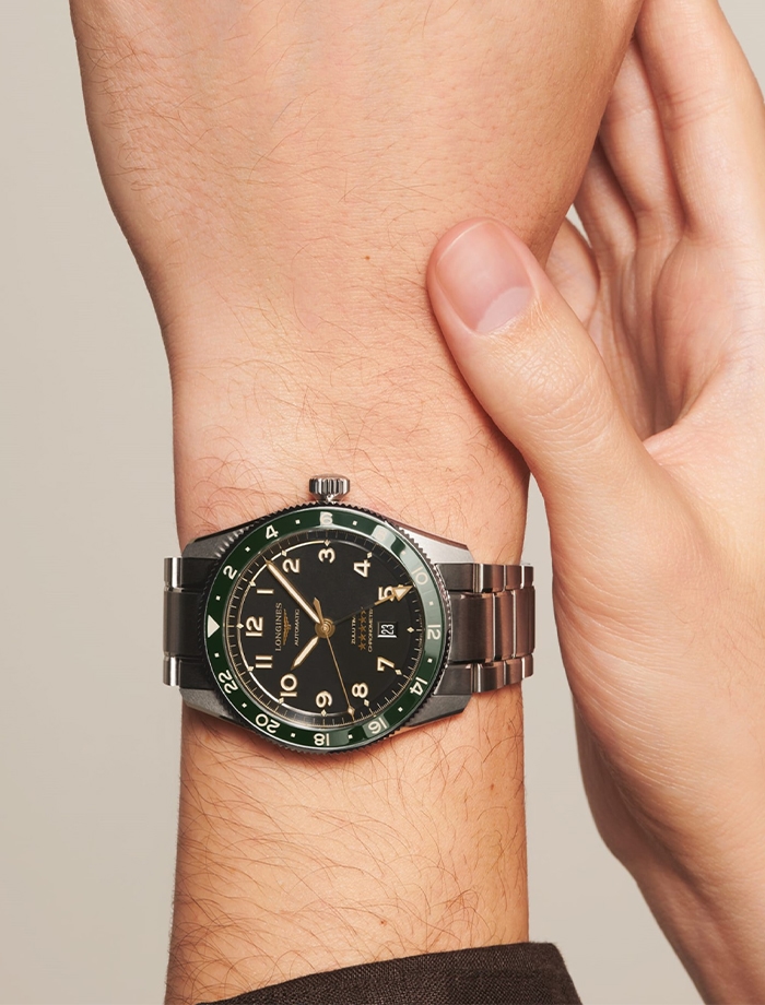 Longines men&#39;s watch with black dial, green bezel and stainless steel bracelet on a wrist.