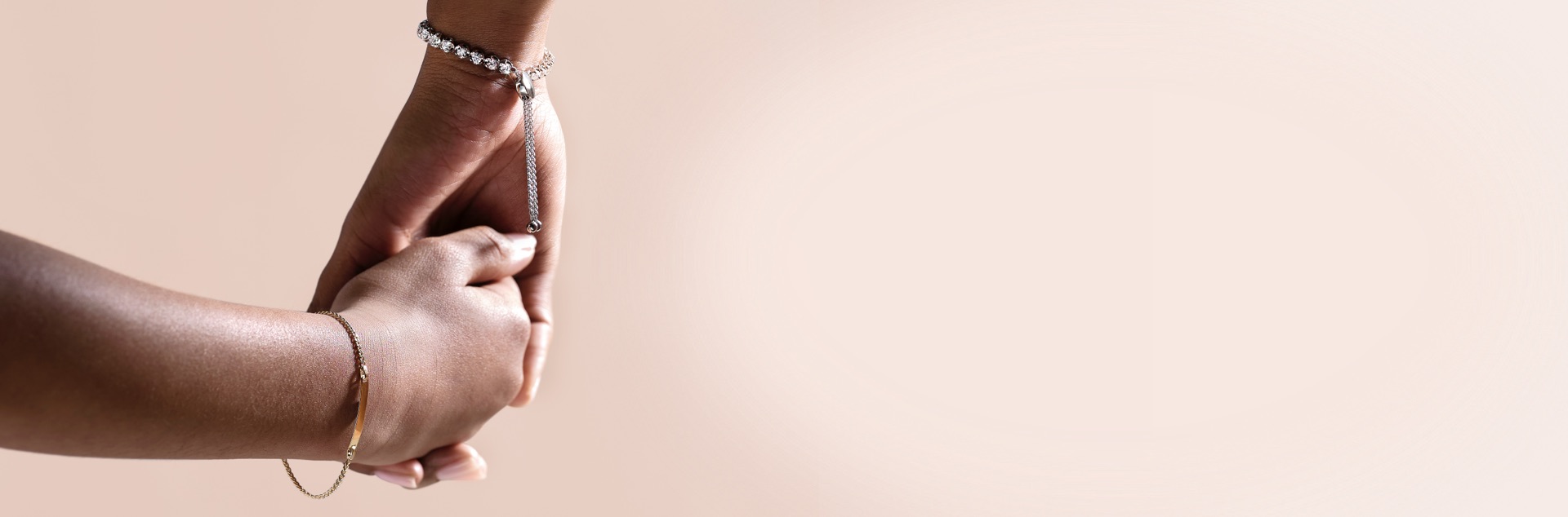 Mother and child holding hands wearing bracelets from Jared with a soft pink background.