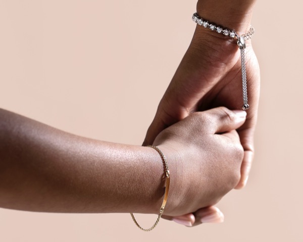 Mother and child holding hands wearing bracelets from Jared with a soft pink background.