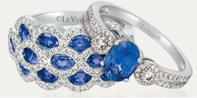 Two Le Vian Sapphire and diamond rings, one 3 stone diamond with a sapphire center stone, and the other a sapphire cluster with diamond halos, on a gray background.