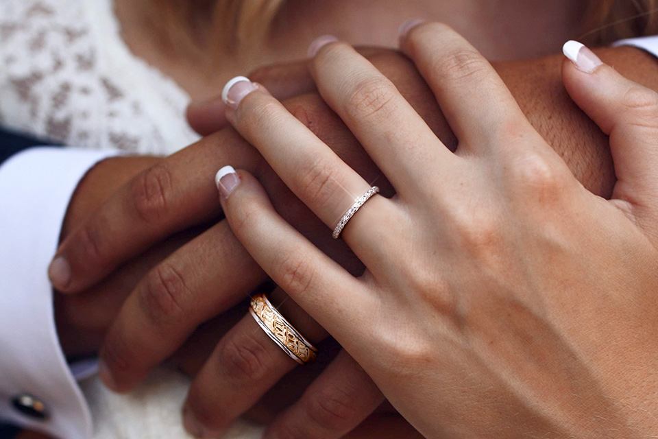 Man and woman's hands, both wearing Y Knot wedding bands