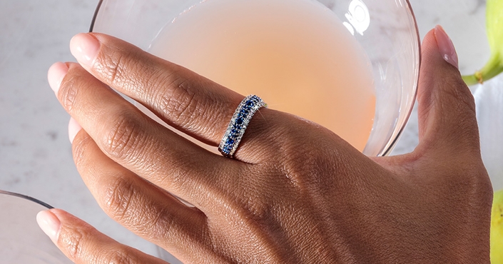 Image of a hand wearing a blue sapphire engagement ring hovering over a martini.