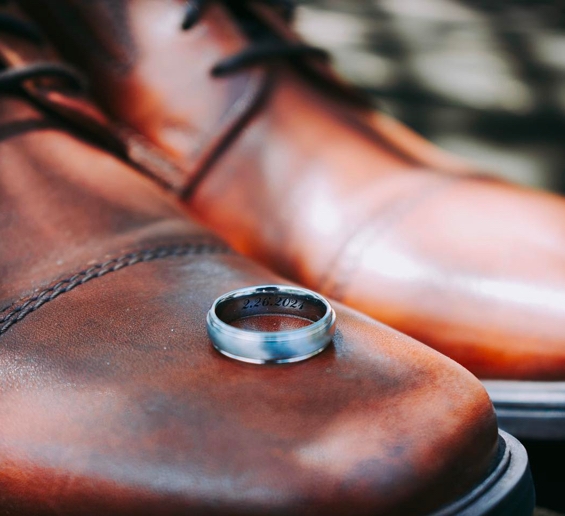 Mens ring with a date engraved on the inside of the band sitting on a pair of leather dress shoes
