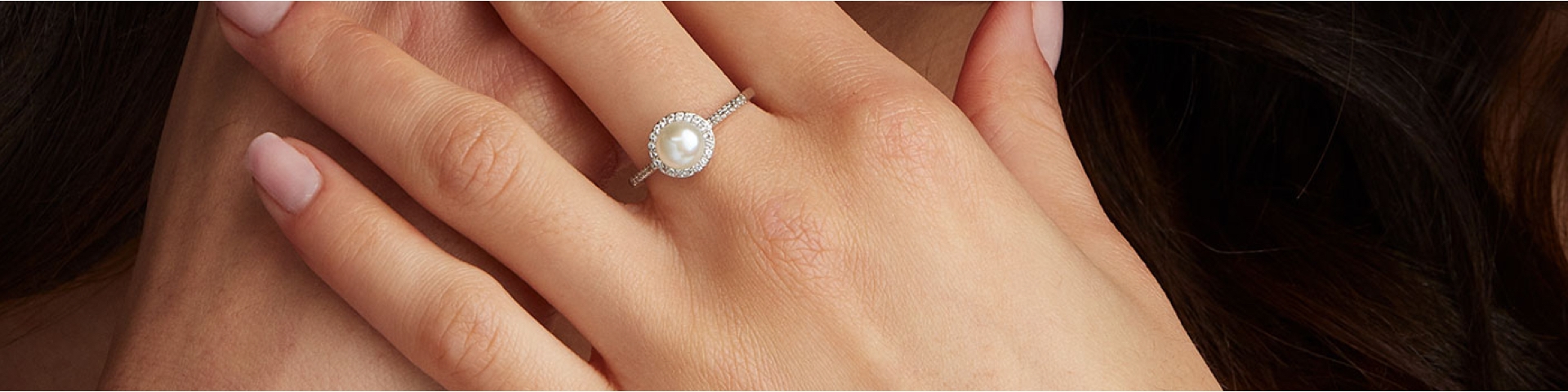 Woman wearing a cultured pearl ring with diamond halo on her finger.