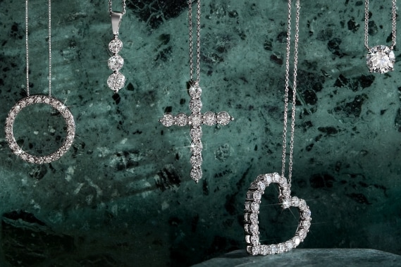 Image of diamond pendant necklaces hanging in front of a jade green background.